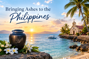 Cremation urn with white plumeria flowers on a rock by the sea near a coastal church, with the title Bringing Ashes to the Philippines